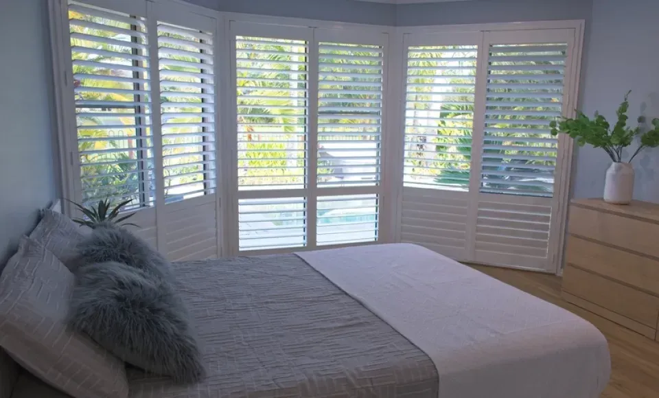 A bedroom with a bed , dresser , and shutters on the windows.