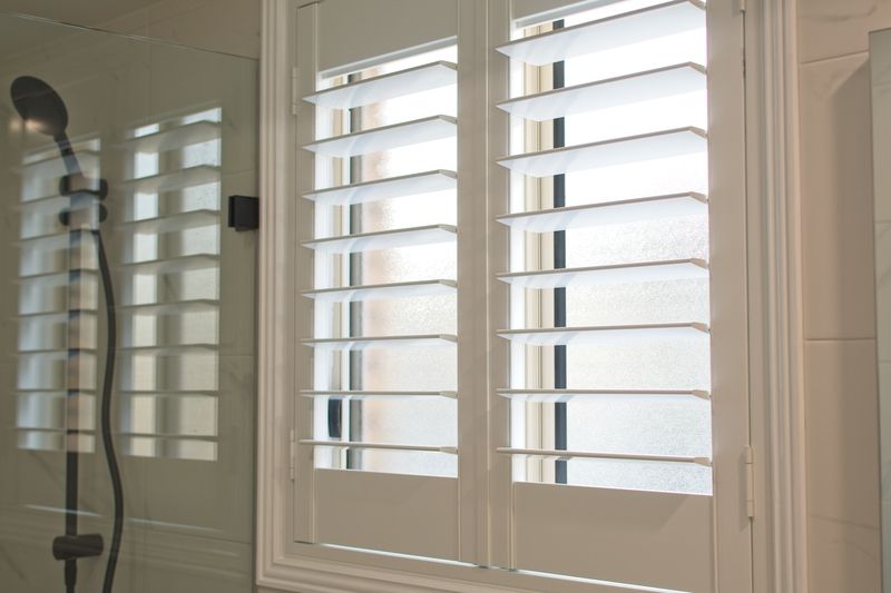 A bathroom with white shutters and a shower head