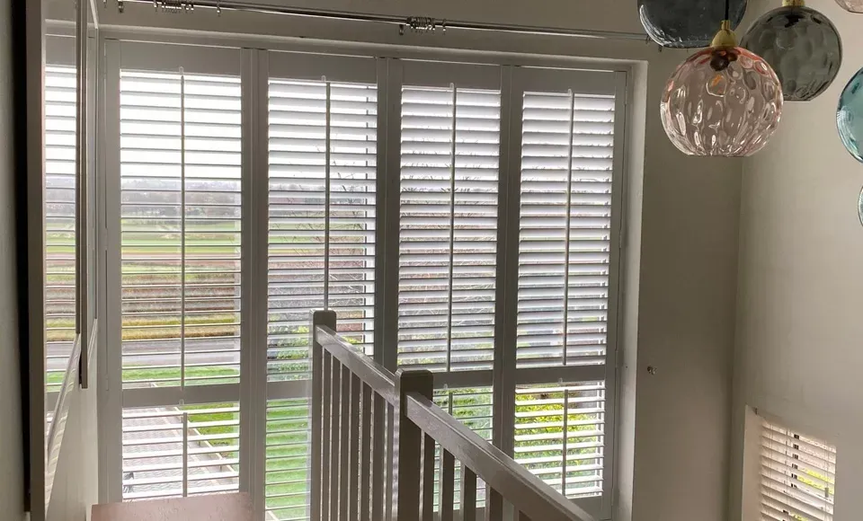 A staircase with shutters on the windows and a ceiling light.