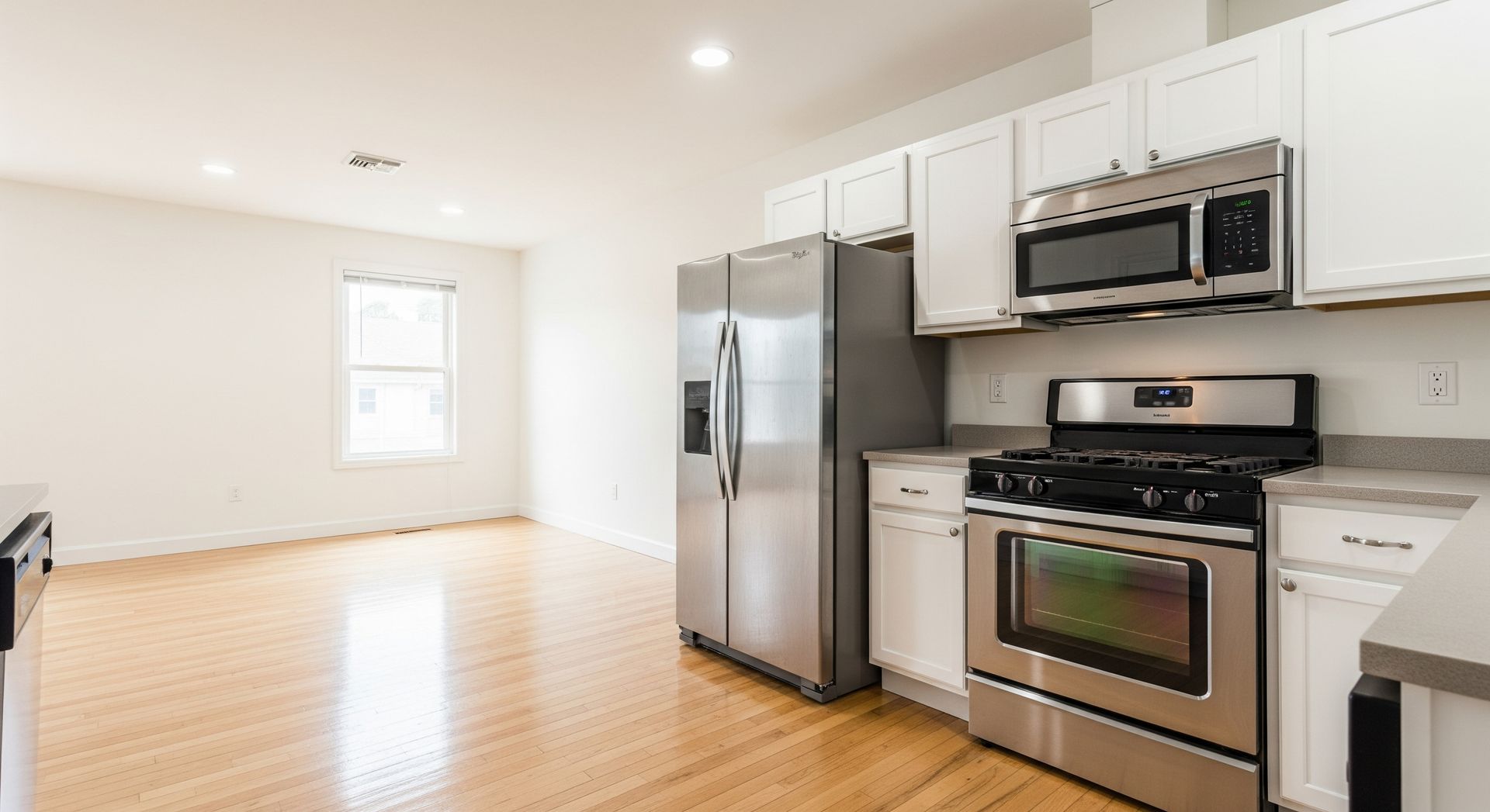 Bright kitchen with stainless steel appliances, white cabinets, and wooden floor.