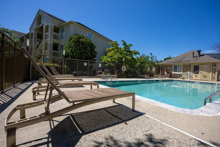 A large swimming pool surrounded by lawn chairs in front of a building.