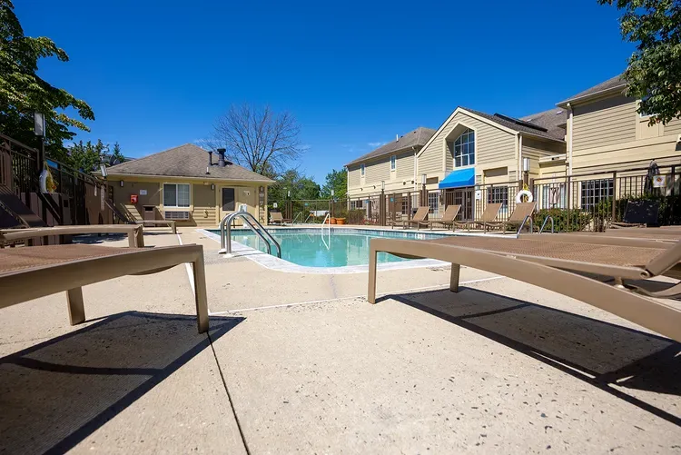A large swimming pool is surrounded by chairs and a building.