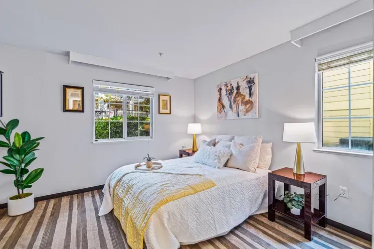 A bedroom with a bed , two lamps , a plant and a window.