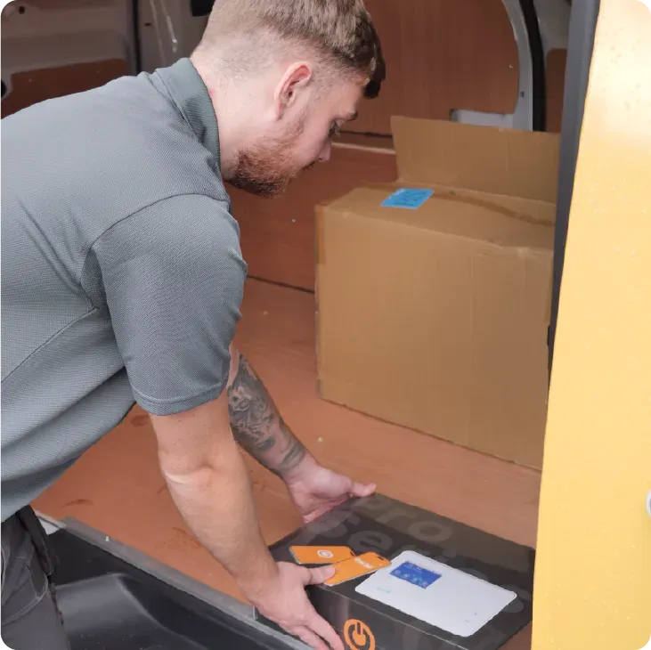 Man loading a package into a van with other boxes on a wooden floor, yellow interior.