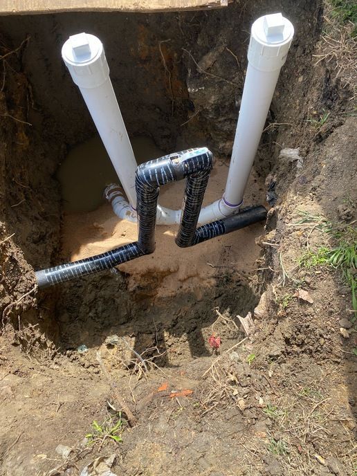 A bunch of pipes are laying in the dirt in a hole.