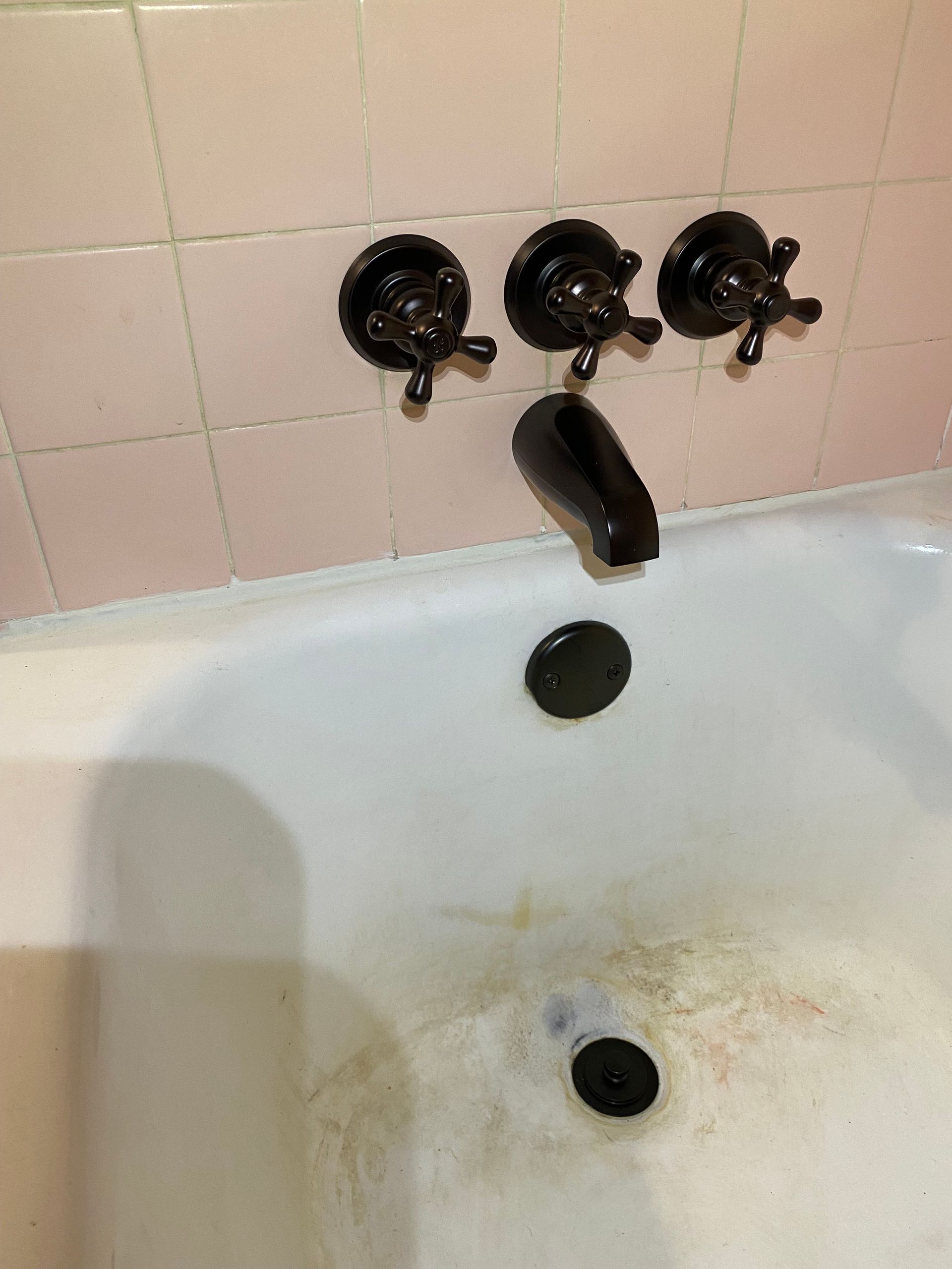 A bathtub with black faucets and a pink tile wall.