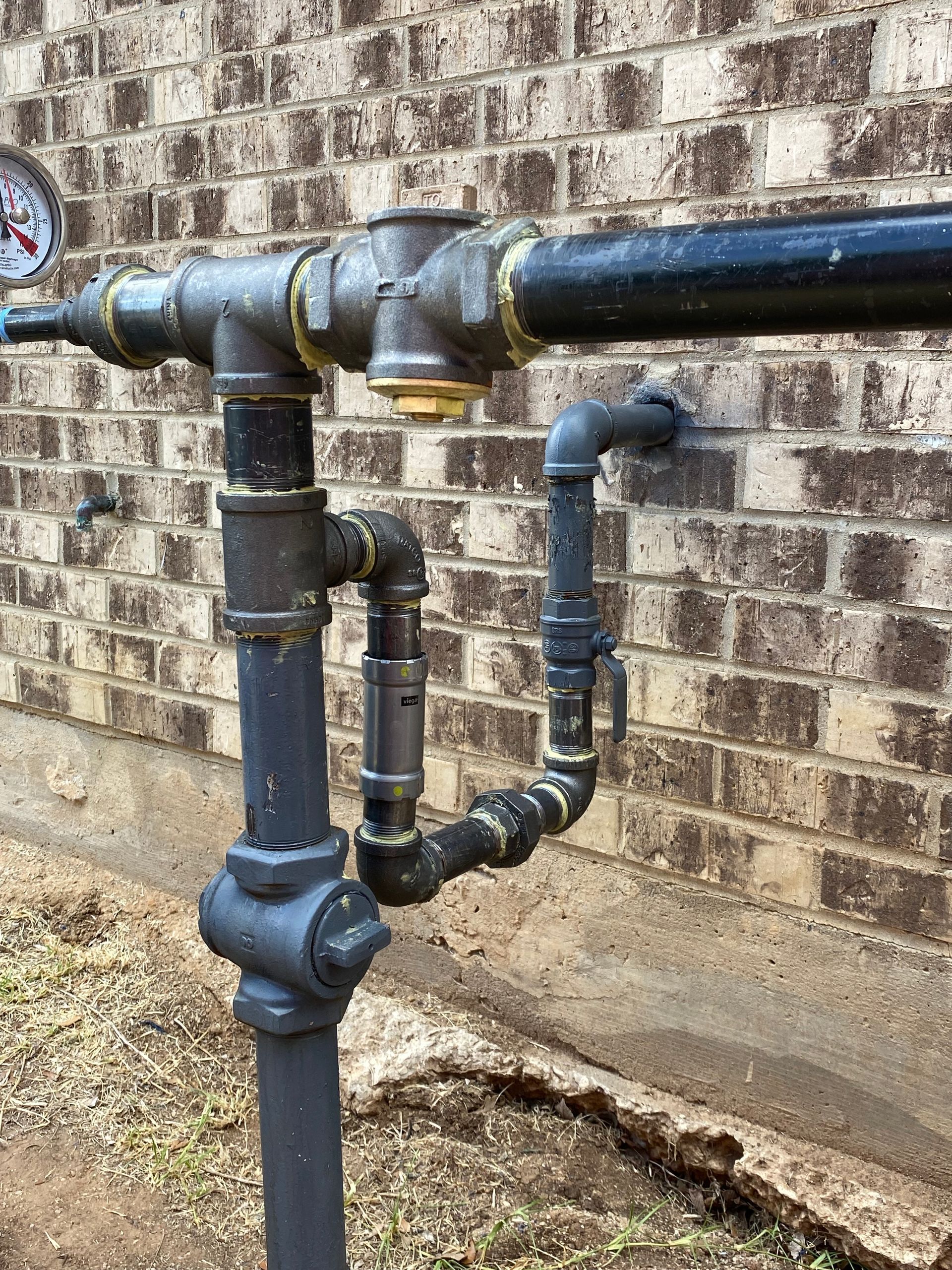 A close up of a pipe with a gauge attached to it in front of a brick wall.