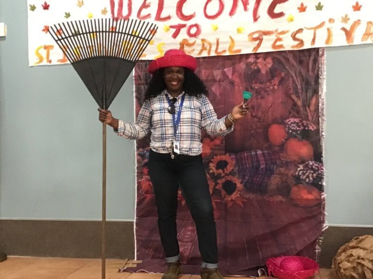 A woman is holding a rake in front of a sign that says welcome to fall festival