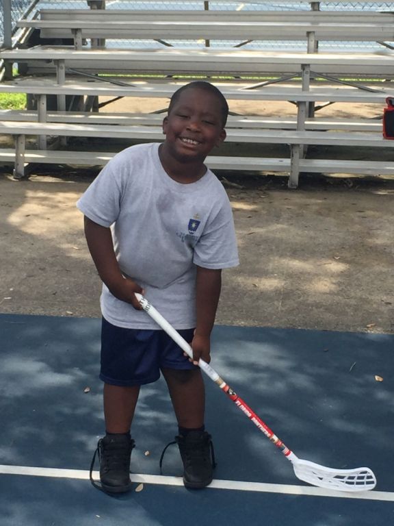 A young boy holding a lacrosse stick on a court