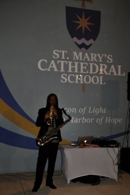 A man playing a saxophone in front of a sign for st. mary 's cathedral school