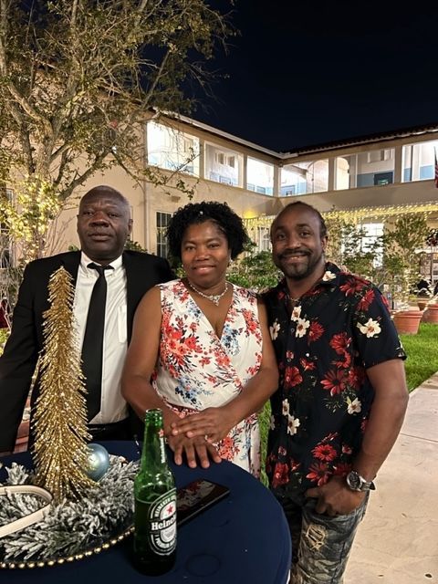 Two men and a woman are posing for a picture with a bottle of heineken beer on a table.