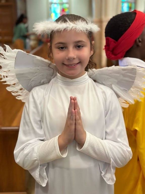 A young girl dressed as an angel with her hands folded in prayer.