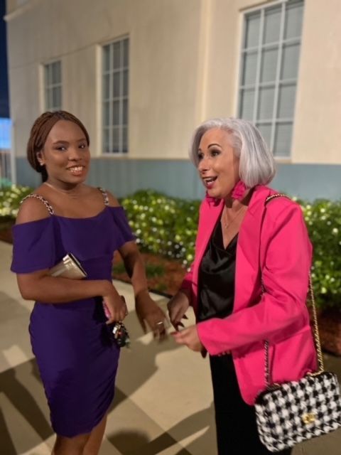 A woman in a purple dress and a woman in a pink jacket are standing next to each other.