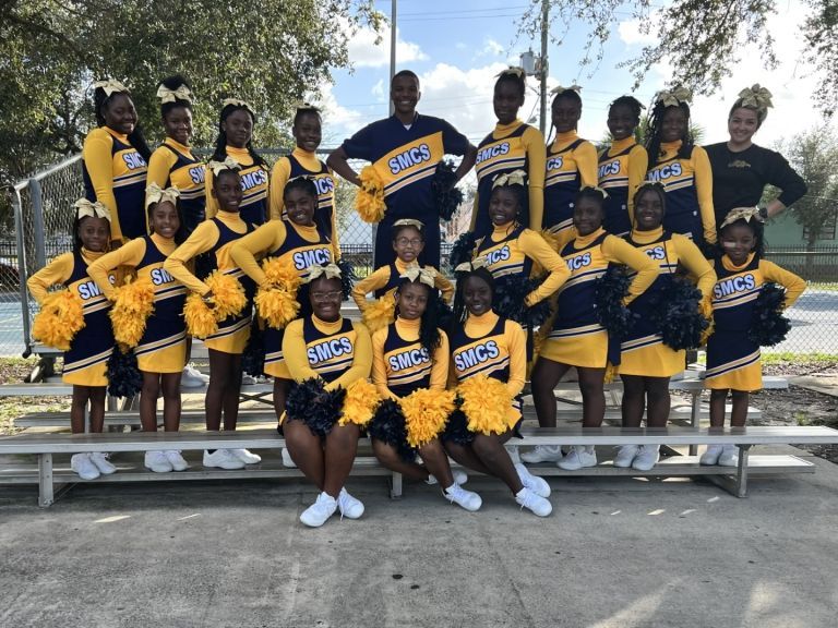A group of cheerleaders are posing for a picture with their coach