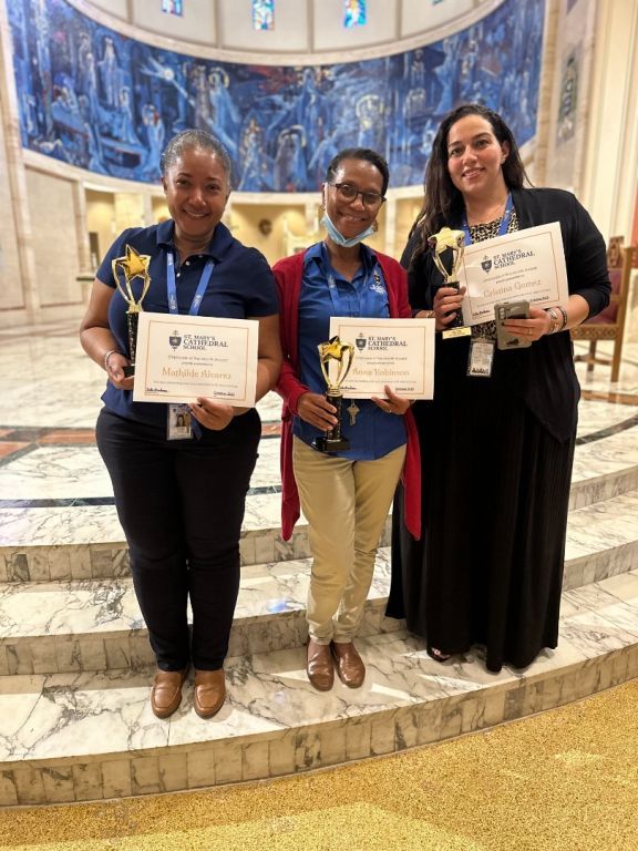 Three women are holding trophies and certificates in a church.