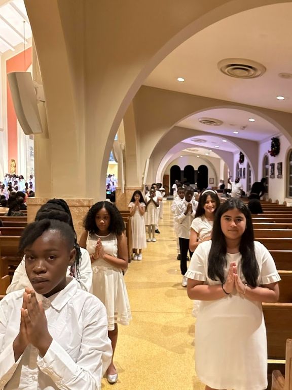 A group of children in white dresses are praying in a church.