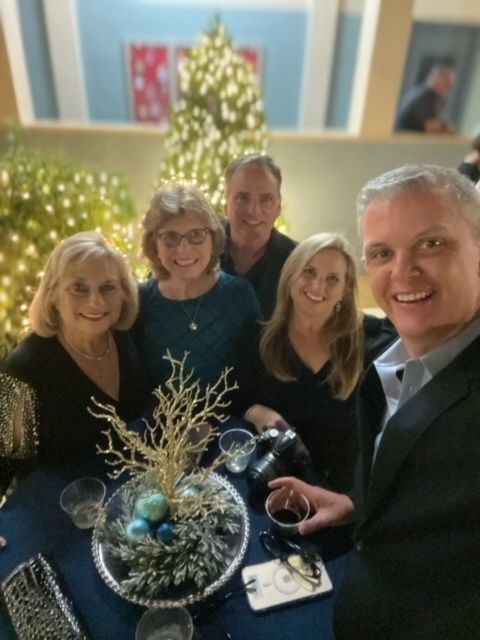 A group of people sitting around a table with a christmas tree in the background