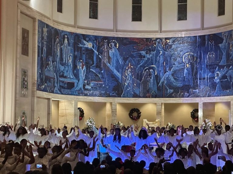 A large group of people are standing in front of a large painting on the wall.