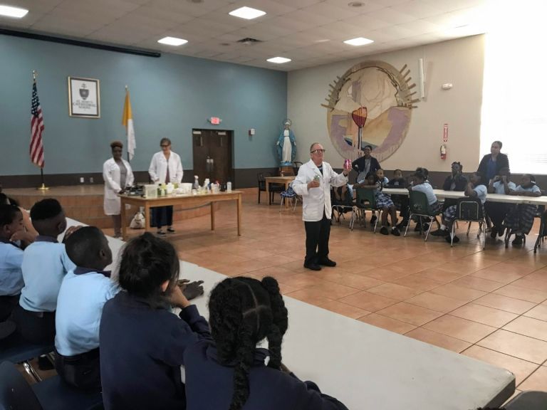 A man in a lab coat is giving a presentation to a group of children
