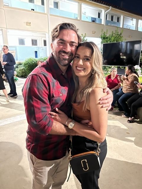 A man and a woman are posing for a picture in front of a building.