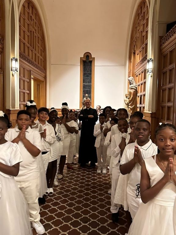 A group of children are standing in a church with their hands folded in prayer.