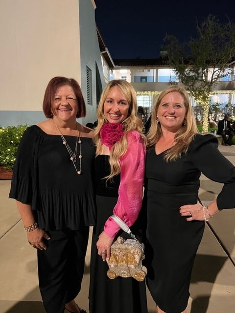 Three women are posing for a picture in front of a building at night.