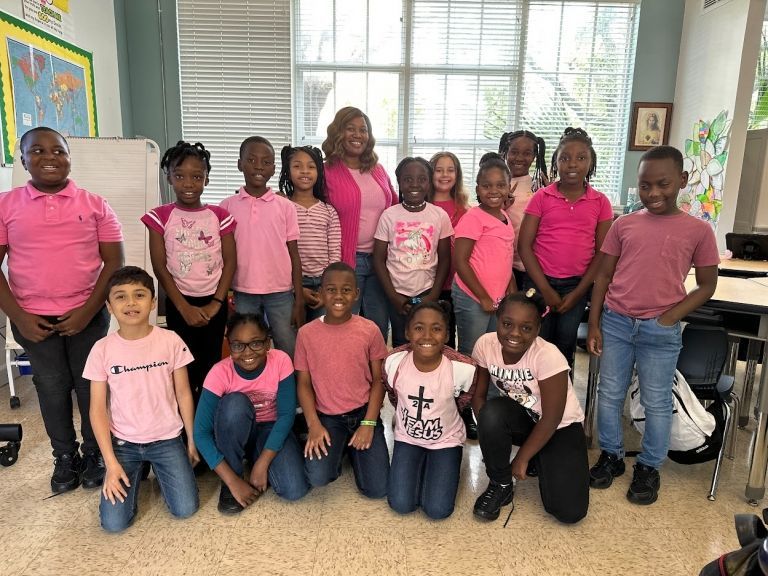 A group of children wearing pink shirts are posing for a picture in a classroom.