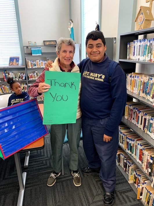 A boy and a woman are standing in a library holding a thank you sign
