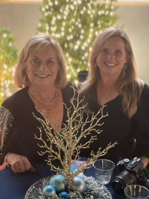 Two women are sitting at a table with a christmas tree in the background