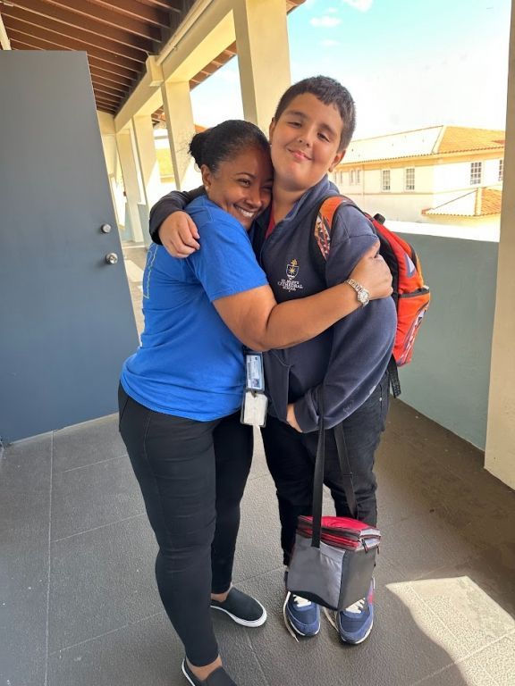 A woman in a blue shirt is hugging a boy with a backpack