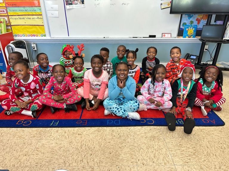A group of children in pajamas are sitting on the floor in a classroom.