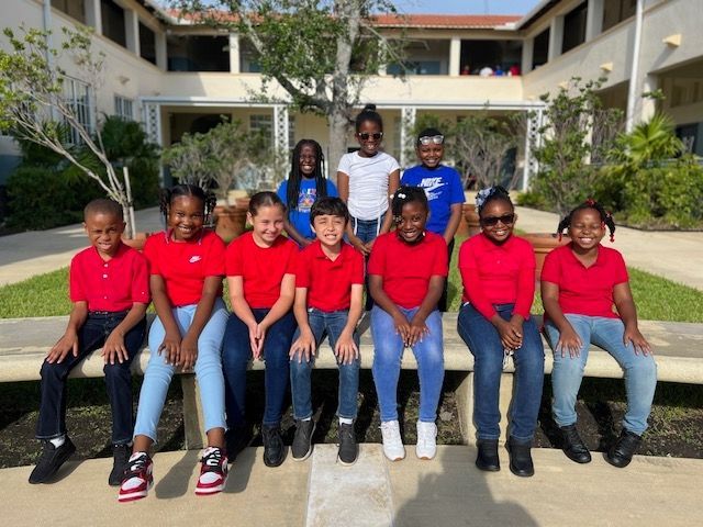 A group of children in red shirts are sitting on a bench in front of a building.