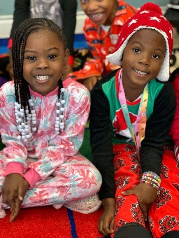 Two young girls are sitting on the floor wearing pajamas and hats.