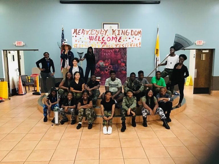 A group of people are posing for a picture in front of a sign that says heavenly kingdom welcome.