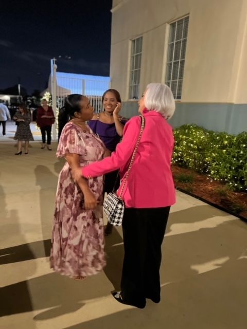 A woman in a pink jacket is hugging two other women