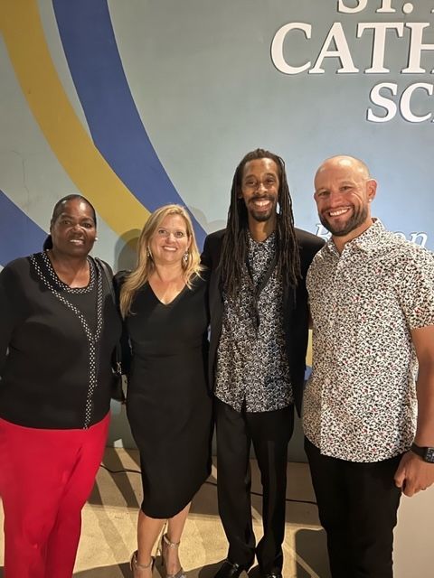 A group of people are posing for a picture in front of a wall that says cath school.