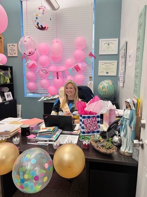 A woman is sitting at a desk decorated with pink balloons