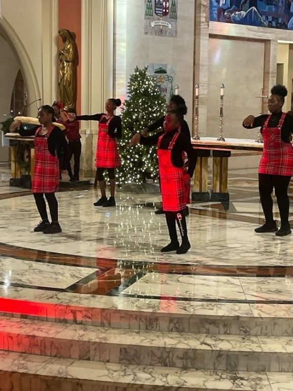 A group of women are dancing in a church in front of a christmas tree.