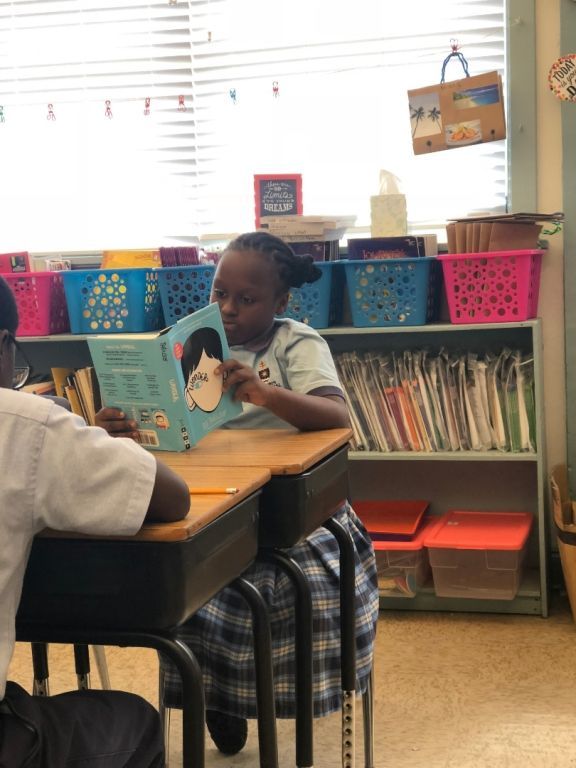 A girl sits at a desk reading a book