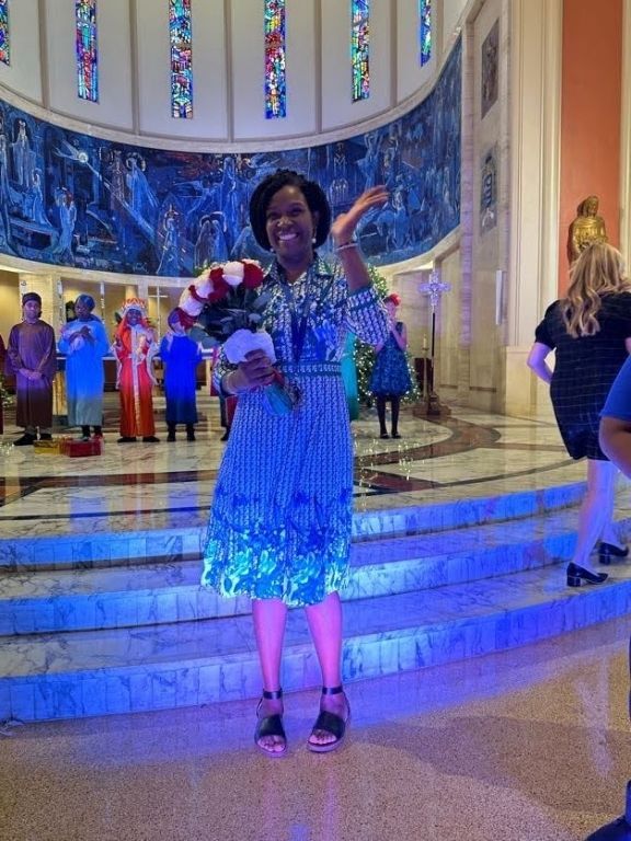 A woman in a blue dress is standing in a church holding a christmas wreath.
