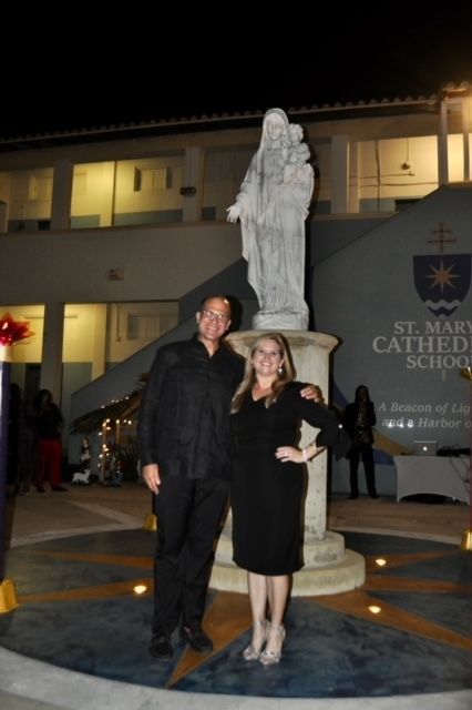 A man and a woman pose in front of a statue in front of st. mary cather school