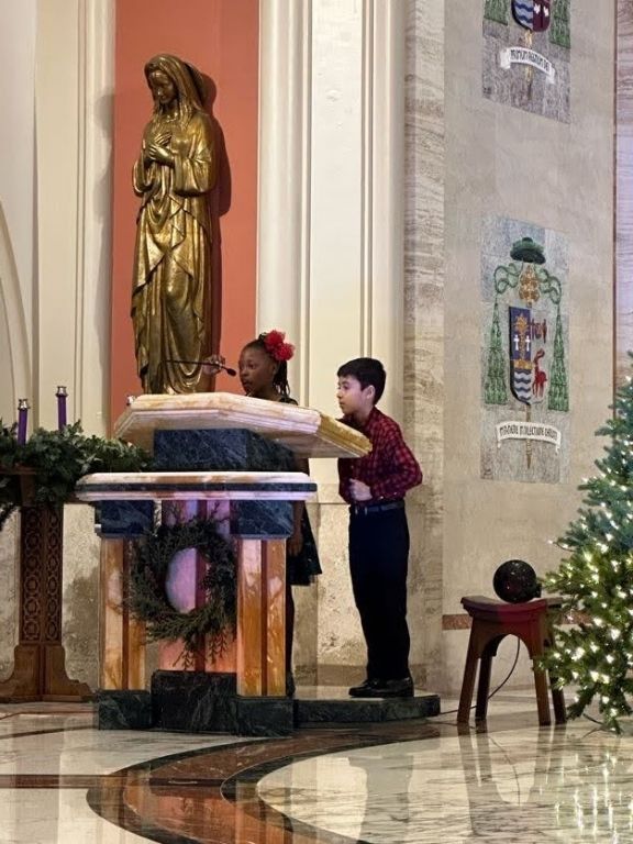 A boy and a girl are standing in front of a statue in a church.