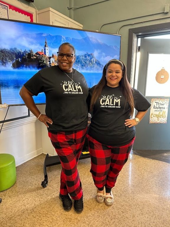 Two women are standing next to each other in front of a large screen.