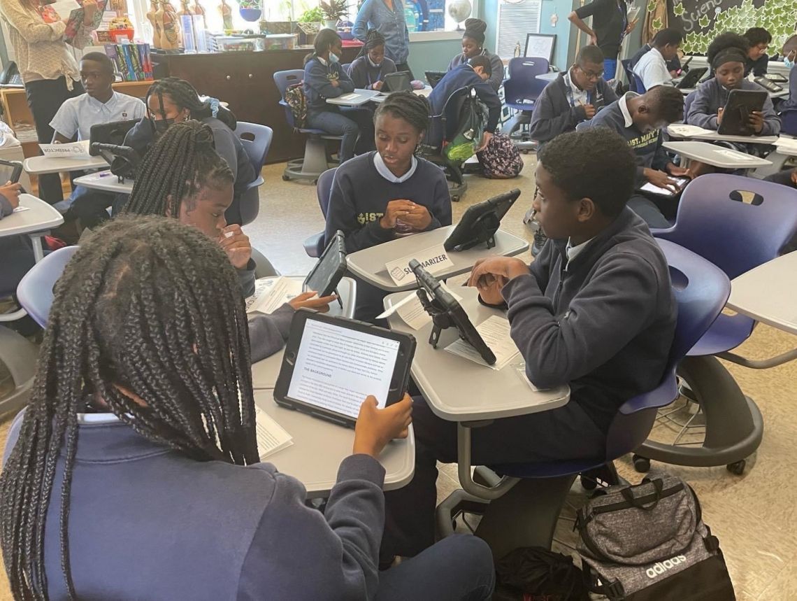 A group of children are sitting at desks in a classroom using tablets.