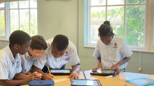 A group of children are sitting at a table looking at tablets.