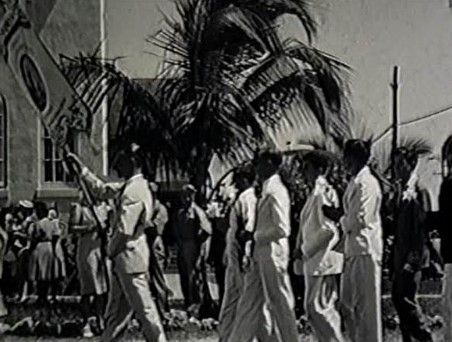 A black and white photo of a group of people walking in front of a church.