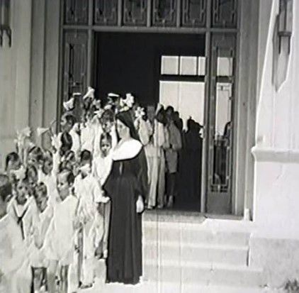 A black and white photo of a group of people standing outside of a building.