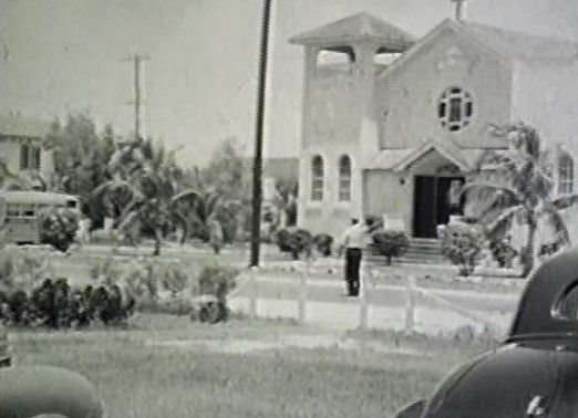 A black and white photo of a man walking in front of a church.