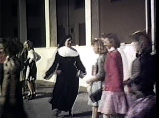 A woman in a nun costume is standing in front of a group of children.