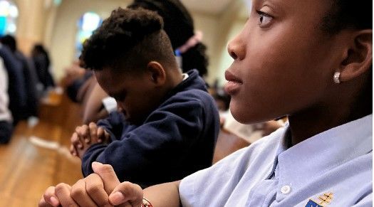 A group of children are sitting in a church with their hands folded in prayer.